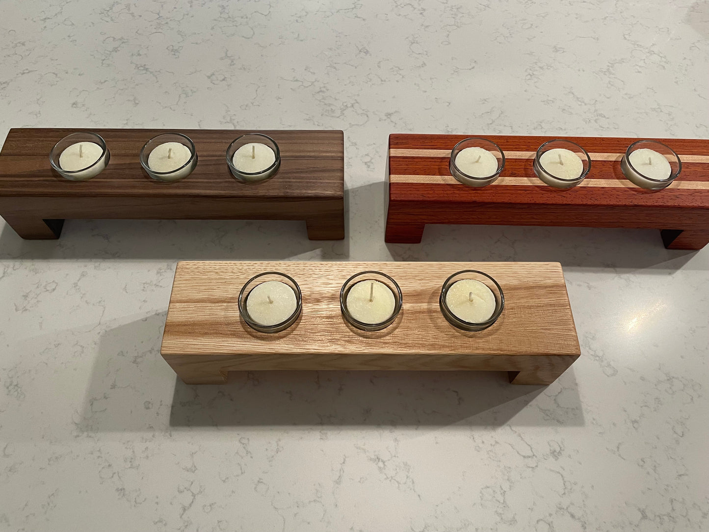 Three wooden candle holders with candles on a light gray surface