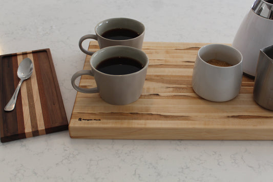 Brown maple cutting board with coffee cups and carafe.