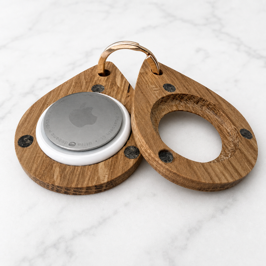 A pair of wooden keychain organizers with a teardrop shape, shown on a white marble background. One piece has a circular magnetic pocket holding a silver Apple AirTag, and the other has a cutout ring design.