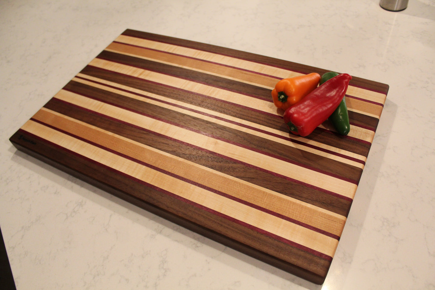 Large Wood Cutting Board, made from a unique blend of Walnut, Maple, Cherry, and Purpleheart strips shown with assortment of peppers.